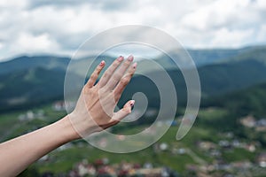 Female hand on nature background. reach the mountains. Travel manicure