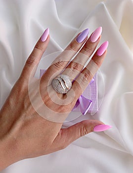 Female hand with a nice manicure and a large ring with white stones and gold stripes