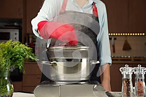 Female hand open lid of steel cooking pan on electric hob with boiling water
