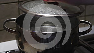Female hand opening the glass lid of the steel pan with boiling water. Selective focus