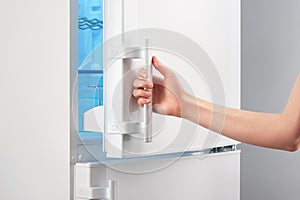 Female hand opening white refrigerator door on gray