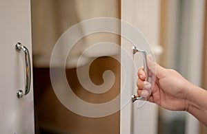 Female hand opening white wardrobe doors with the walkin closet style and copy space behind the doors inside the house photo