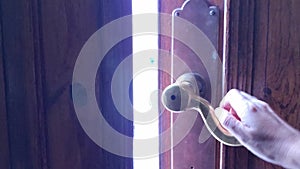 Female hand opens antique brass door handle and pushes old wooden door to outside for exit