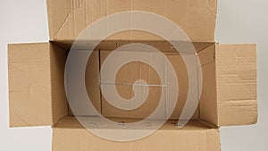 Female hand opens brown cardboard box and fills with white filler for safe transportation, top view