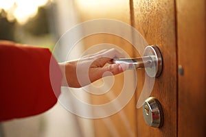 A female hand opens a brown wooden door by clicking on a chromed handle
