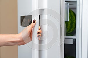 Female hand opens door of a fridge