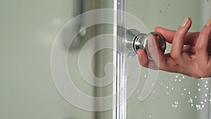 Female hand opens the door in the shower cabin. Woman hold handle bathroom cabin with right hand. Detail of a modern