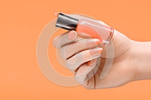 Female hand with orange nail design. Orange nail polish manicure. Woman hand hold orange varnish on orange background