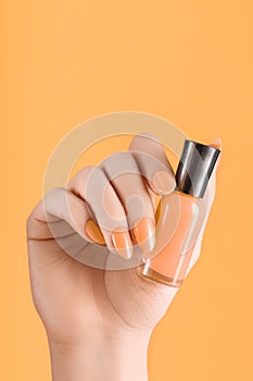 Female hand with orange nail design. Orange nail polish manicure. Woman hand hold orange varnish on orange background