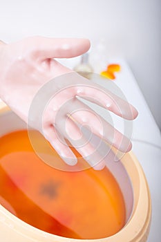 Female hand orange parrafin wax in bowl.