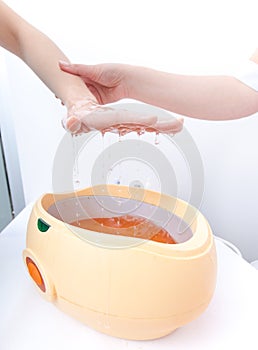 Female hand orange parrafin wax in bowl. Manicure beauty spa salon