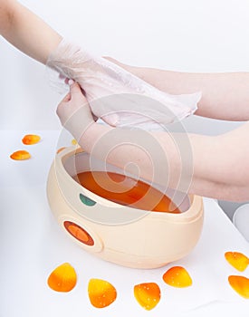 Female hand orange parrafin wax in bowl. Manicure beauty spa salon