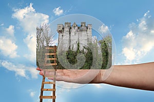 Female hand outstretched against beautiful summer landscape, blue sky with clouds, ancient castle, a wooden staircase in the palm