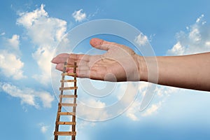 Female hand outstretched against beautiful summer landscape, blue sky with clouds, wooden staircase in palm, concept of