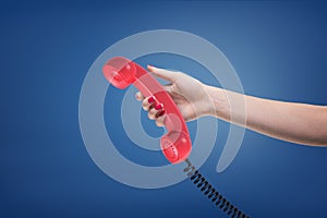A female hand with painted nails holds a red retro phone receiver with a black cord.