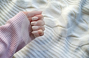 A female hand with a pastel manicure on a knitted sweater background.