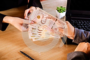 Female hand paying cash ,salary to employee ,hand giving and receiving money or bonus in Thai baht at workplace