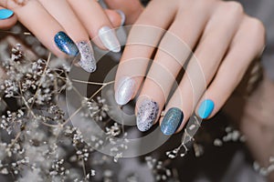 Female hand with pearly nail design. Glitter blue nail polish manicure. Woman hand with white dried flower