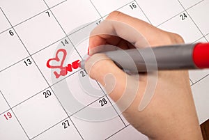 Female hand with pencil drawing heart and word love in calendar for Valentines day