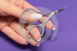 Female hand with perfect manicure holds nail scissors. Manicure scissors  on a purple background