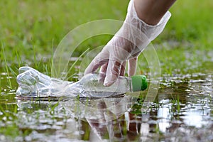 Female hand pick up plastic bottle from the puddle of water in the forest.