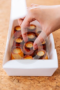 Female hand picking fresh baked CanelÃ©s inside white paper box. A small French pastry flavored with rum and vanillaà¹ƒ
