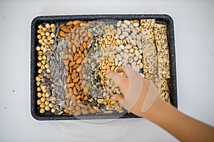 Female hand picking nuts from a black tray with seeds and nuts photo