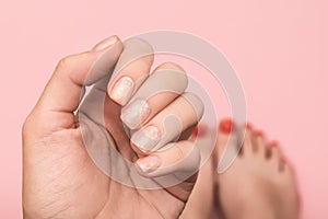 Female hand with pink design. Glitter pink nail polish manicure. Woman hand on pink background with blured red pedicure