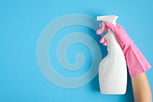 Female hand in pink glove holding cleaning spray bottle on blue background. House cleaning or housekeeping concept