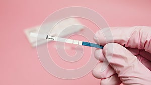 Female hand in a pink medical glove holding positive pregnancy test isolated on pink background. The abbreviation HCG on