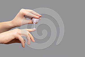 Female hand with pink nail design. Glossy pink fingernails manicure. Woman hand pour purple nail polish on her fingernail on gray