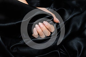 Female hand with pink nail design. Rose glitter nail polish manicure. Woman hand on black fabric background