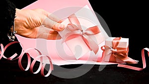 Female hand placing Present box with pink ribbon on the pink and black background,