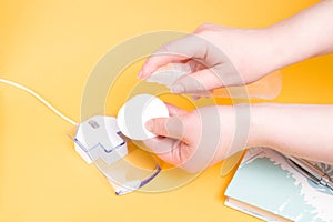 female hand pokes an antiseptic on a cotton pad to wipe a computer mouse, yellow background copy space, workplace hygiene, stay ho