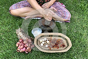 A female hand pounding many kinds of herbs in mortar to make Thai red curry chili paste