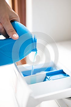 Female hand pouring a blue liquid detergent into a washing machine