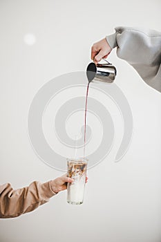 Female hand pouring coffee into glass with milk