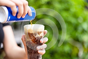 Female hand pouring cola drink from tin to glass