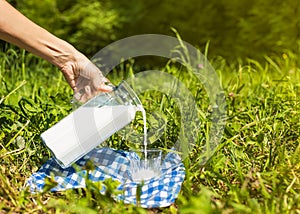 Female hand pouring milk from jug into glass in grass