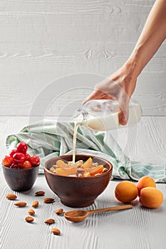 Female hand pouring milk in muesli with apricots and almonds