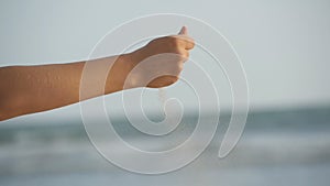 Female hand pouring sea sand through her fingers against an ocean background. Arm of young woman with sand strewed or