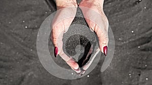 female hand pouring volcanic black sand running through fingers in slow motion at island tropical beach. Beautiful scene