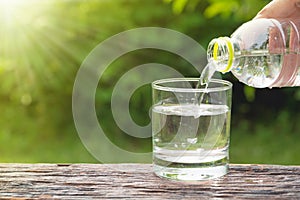 Female hand pouring water from bottle to glass on nature background.