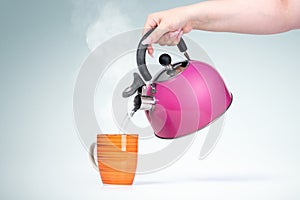 Female hand pours hot water from a pink kettle into a mug with a drink, on light background
