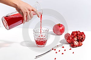 Female hand pours pomegranate juice into a glass. Grenades on a white table