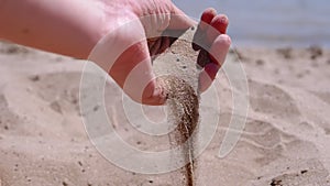 Female Hand Pours Sand Through Fingers on the Beach in the Rays of Sunlight