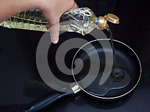 Female hand pours vegetable oil on a frying pan