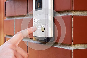 The female hand presses a button doorbell with intercom