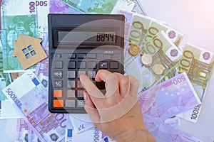 female hand presses buttons on the calculator, against the background of euro banknotes and coins. Small wooden toy