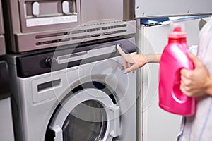 Female hand presses start button on washing machine, holding detergent in hands